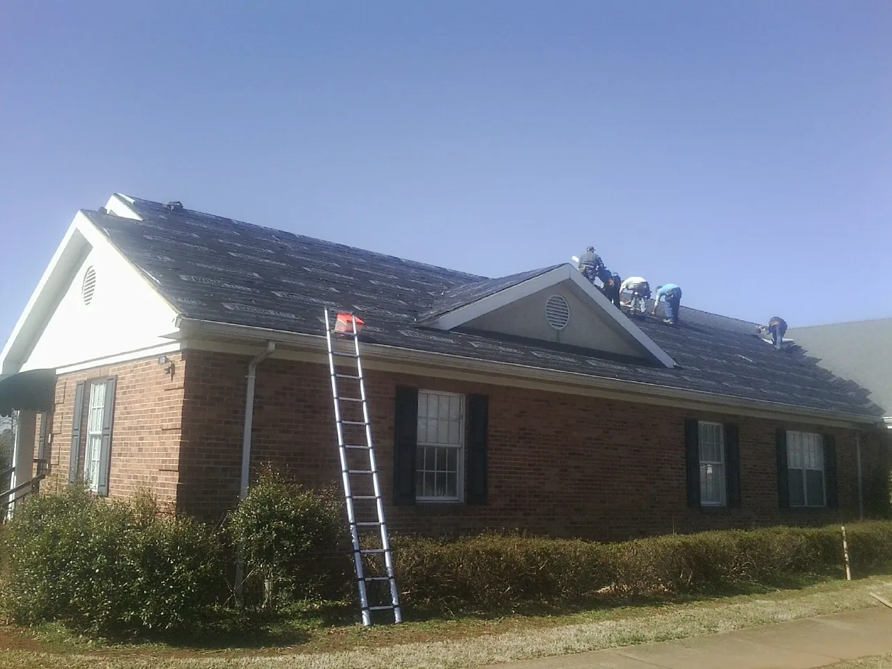 Crew tearing shingles off a brick ranch roof with a ladder set — Emergency Roof Repair work by our crew in Whittaker