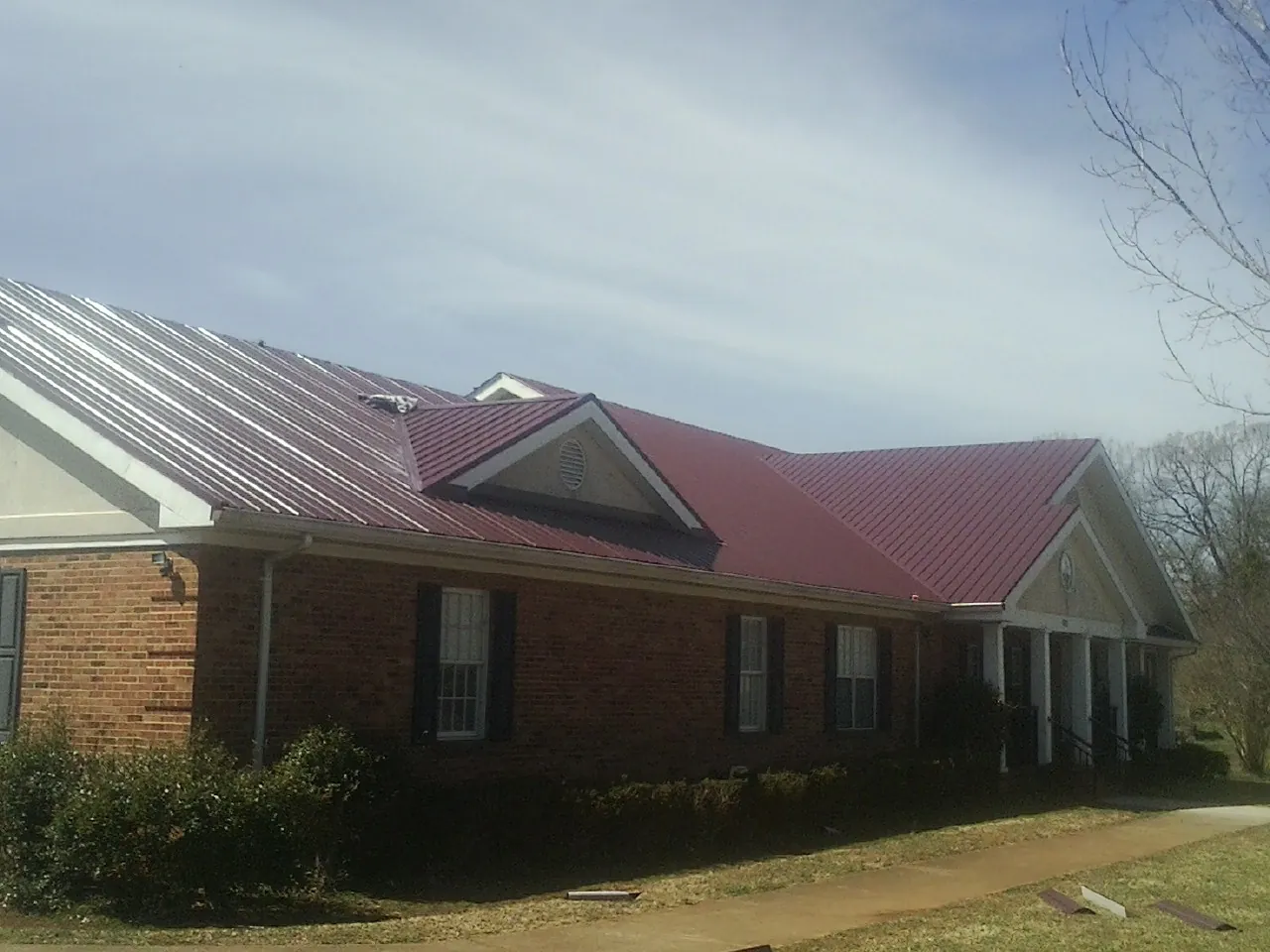 Red metal roof with gabled entries on a long brick building, from a Hail Damage Roof Repair job in Whittaker