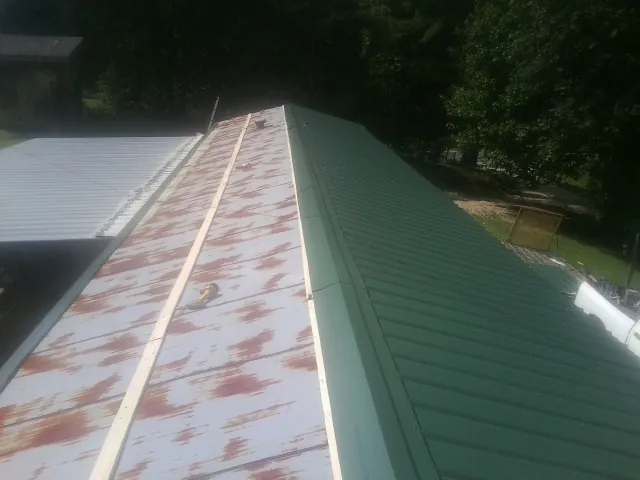 Old rusted panels beside newly installed green metal roofing — Wind Damage Roof Repair by Roofing Brothers in Whittaker