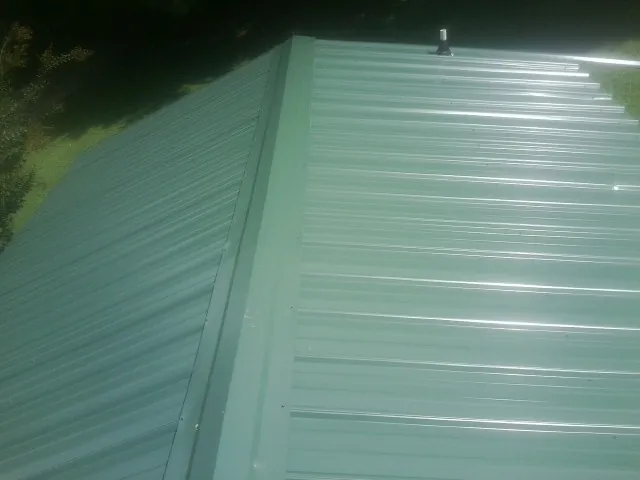 New green metal panels meeting at the ridge of a roof — Flat Roof Repair work by our crew in Whittaker