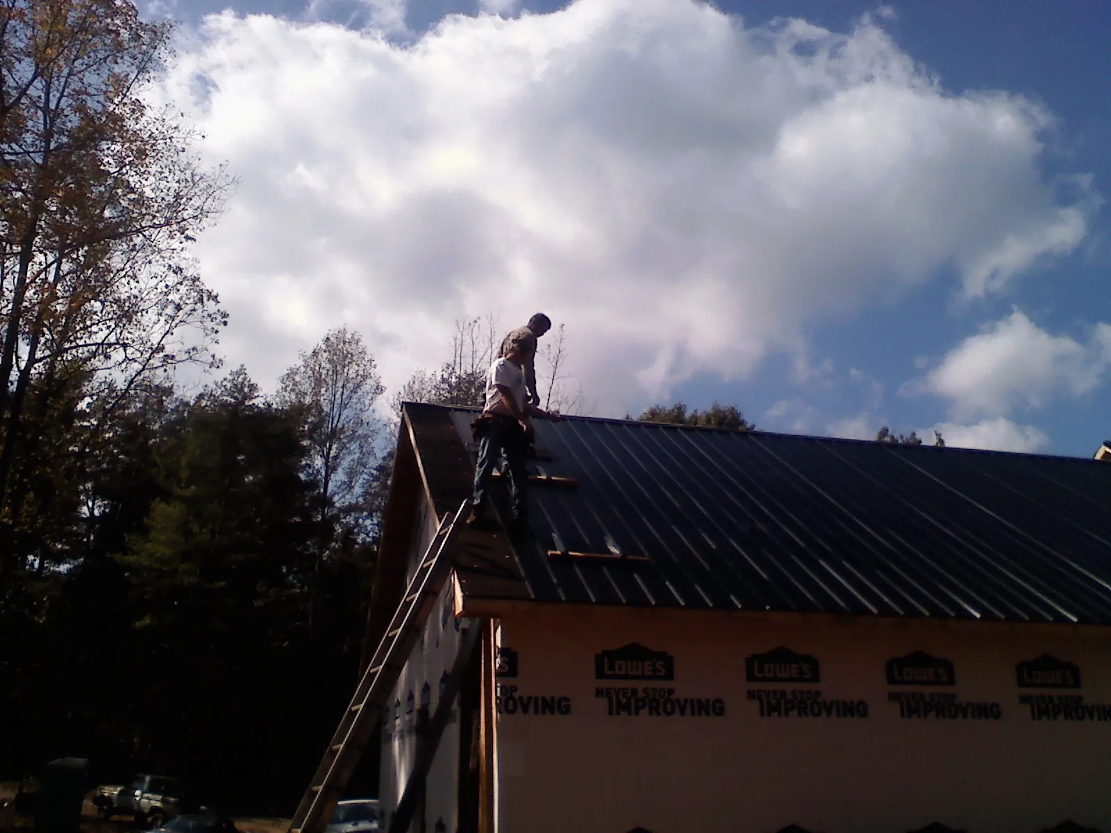 Roofer fastening dark metal panels high against a cloudy sky, from a Roof Inspection job in Whittaker