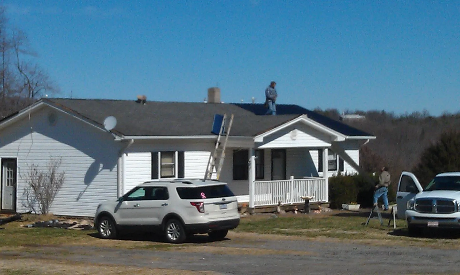 Roofers stripping shingles from a white ranch house roof in Whittaker