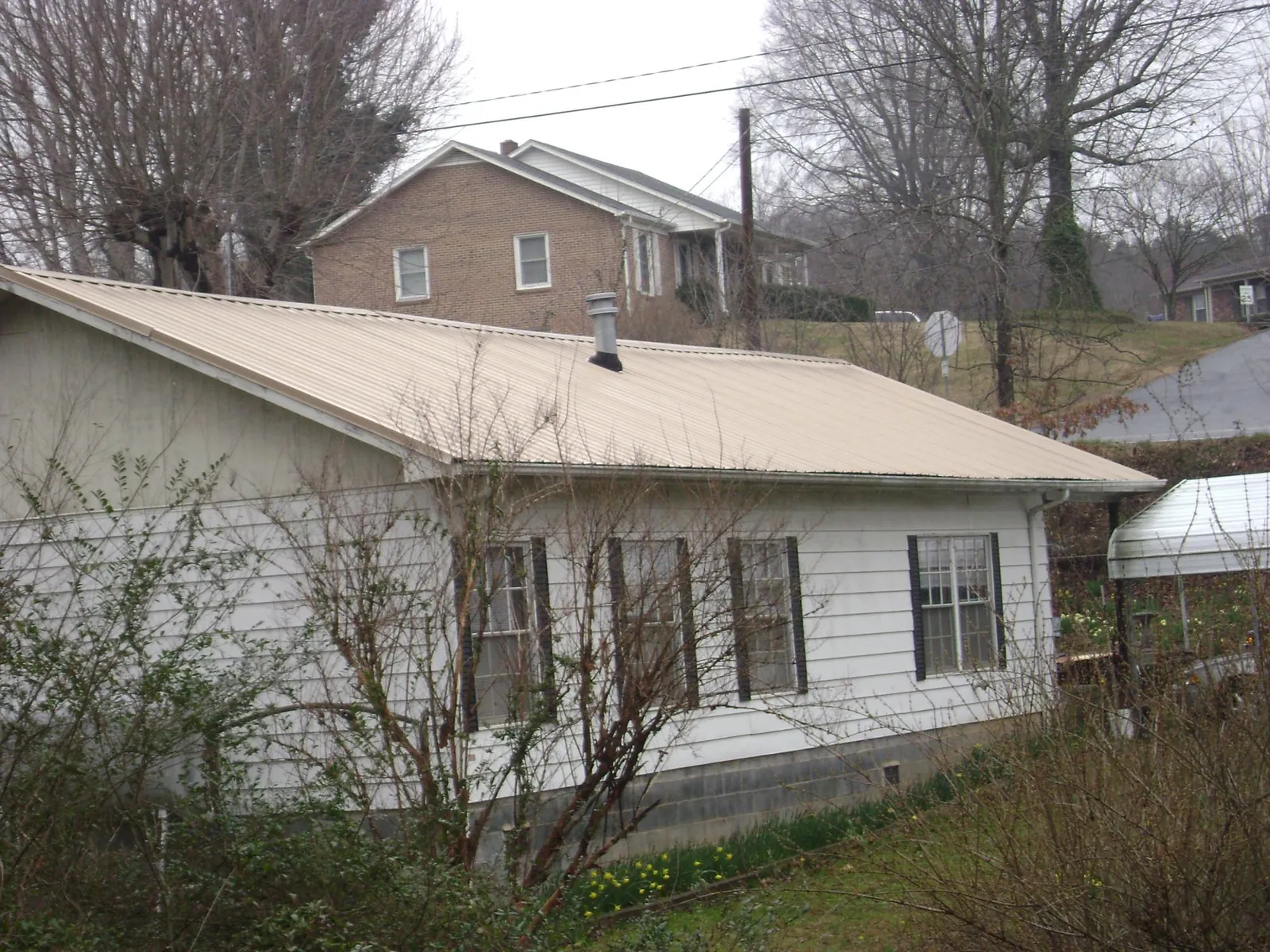 Tan metal roof on a white sided house set into a hillside — Commercial Roofing by Roofing Brothers in Whittaker