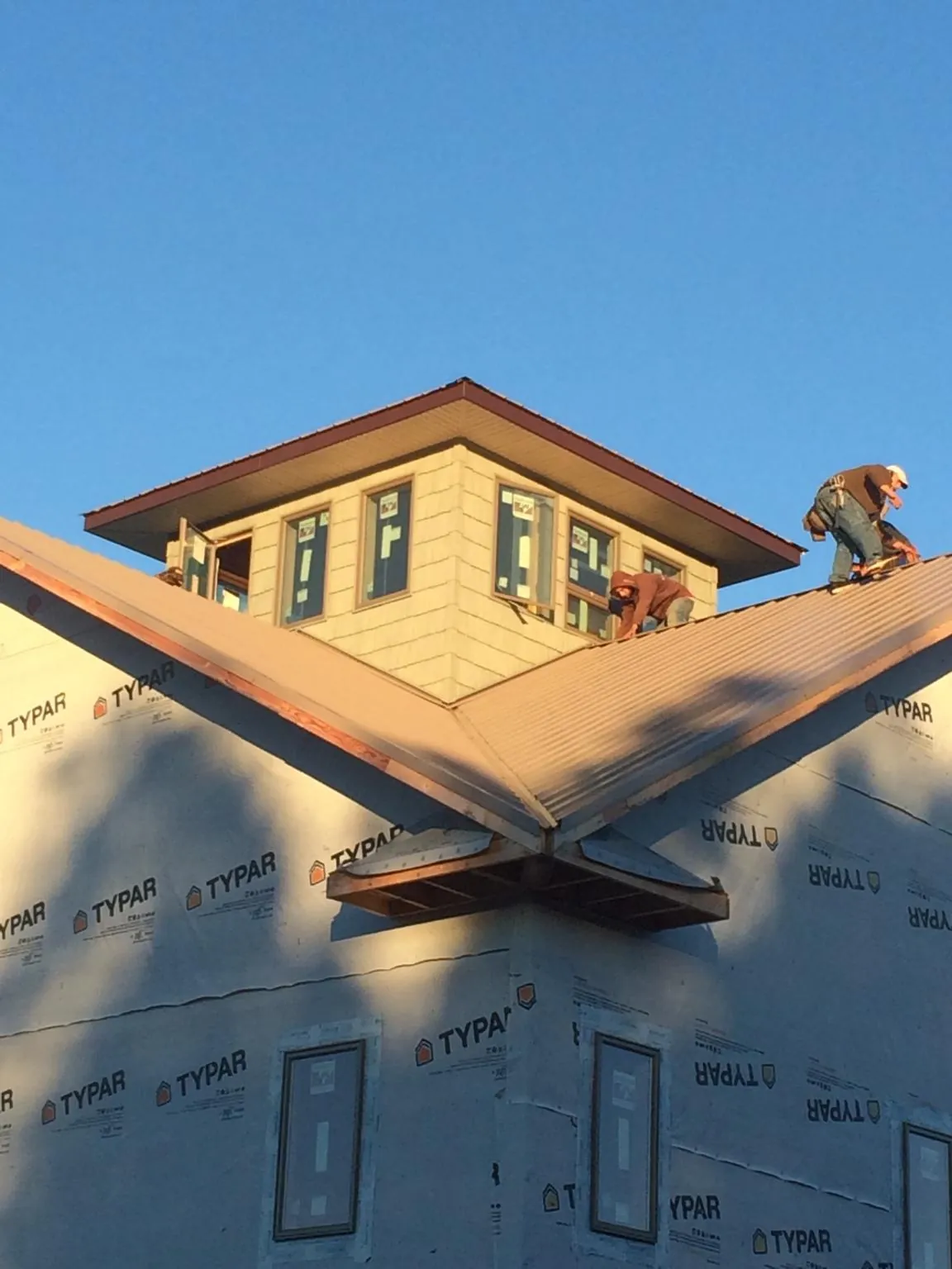 Roofers working around a rooftop cupola on a new metal roof at sunset — Roof Waterproofing in Whittaker by Roofing Brothers